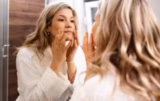 Woman examining perimenopause skin changes in the mirror