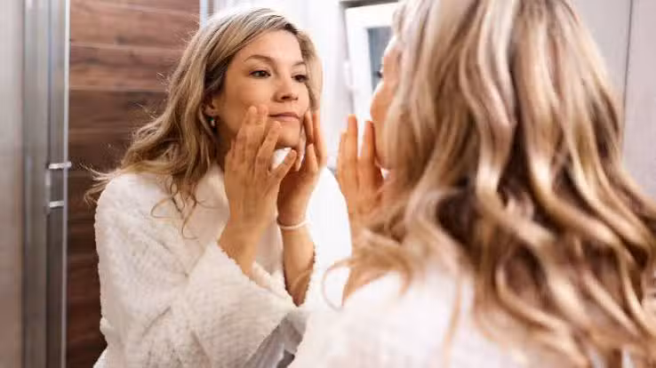 Woman examining perimenopause skin changes in the mirror